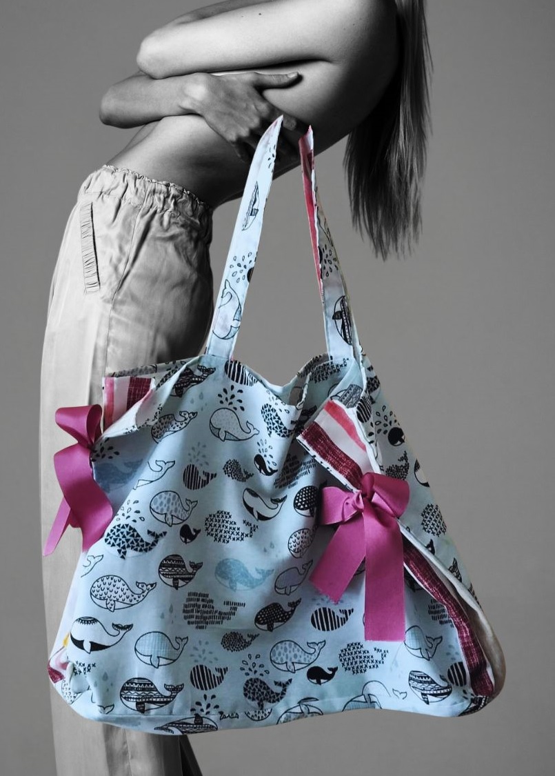 Bolsa de playa de color azul celeste con estampado de ballenas y lazos en los laterales.